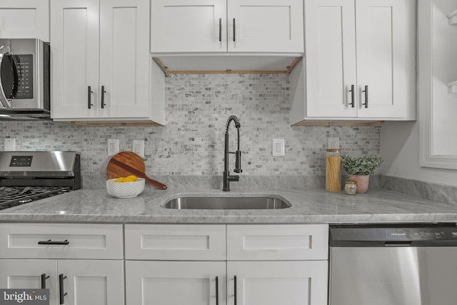 kitchen with tasteful backsplash, stainless steel appliances, sink, and white cabinetry