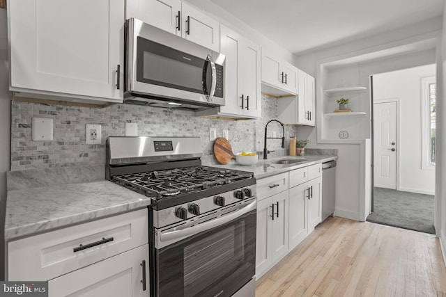 kitchen featuring appliances with stainless steel finishes, sink, light wood-type flooring, white cabinetry, and light stone countertops