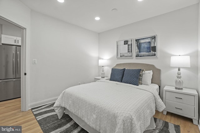 bedroom with light hardwood / wood-style floors and stainless steel refrigerator