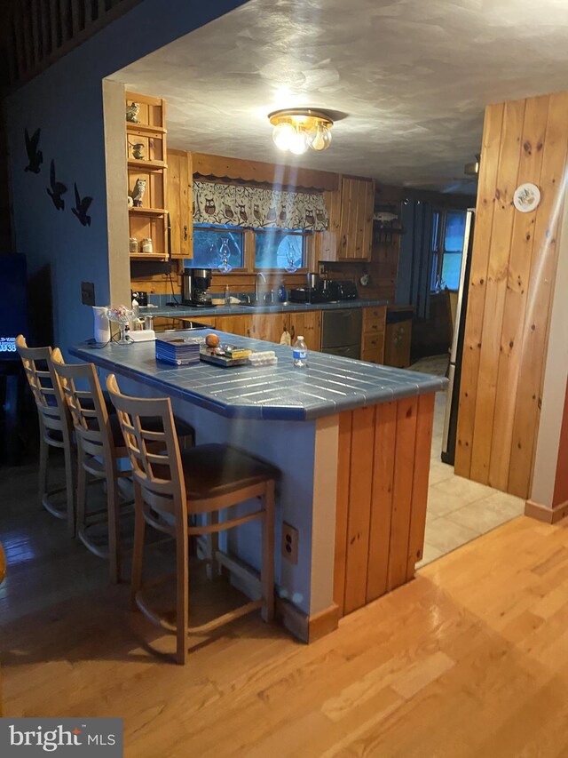 kitchen with kitchen peninsula, sink, light tile floors, a kitchen bar, and tile countertops