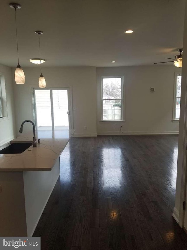 interior space featuring light stone countertops, pendant lighting, dark wood-type flooring, sink, and ceiling fan