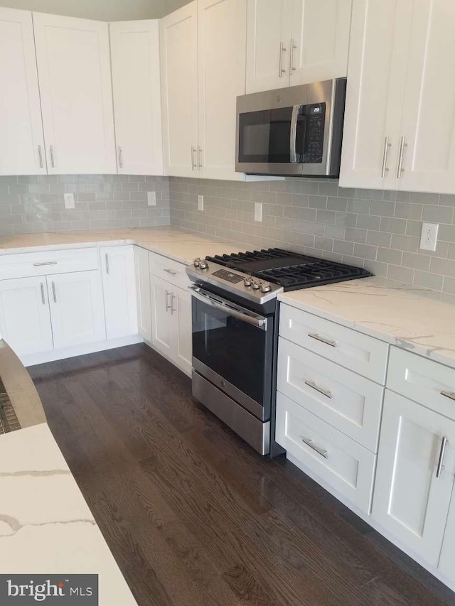 kitchen with stainless steel appliances, decorative backsplash, white cabinetry, and light stone counters