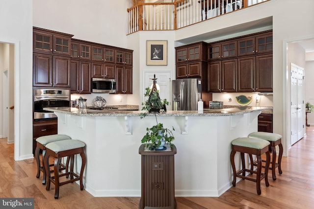 kitchen with light hardwood / wood-style flooring, dark brown cabinetry, stainless steel appliances, and a kitchen bar