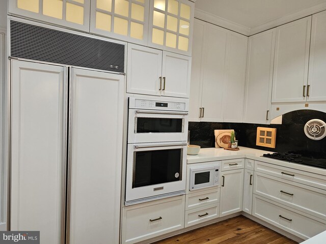 kitchen with wood-type flooring, tasteful backsplash, white cabinetry, and built in appliances