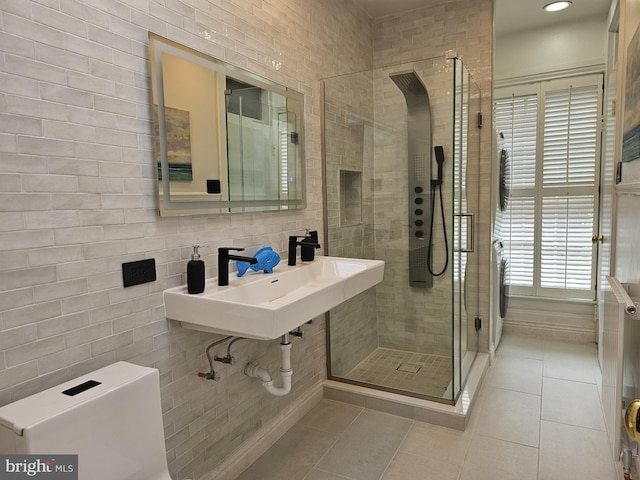 bathroom featuring washer / clothes dryer, tile walls, a shower with shower door, tile flooring, and sink