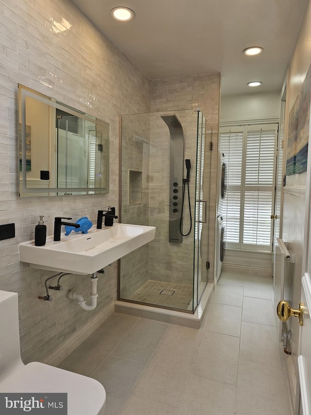 bathroom with a shower with shower door, tile walls, and washer / dryer