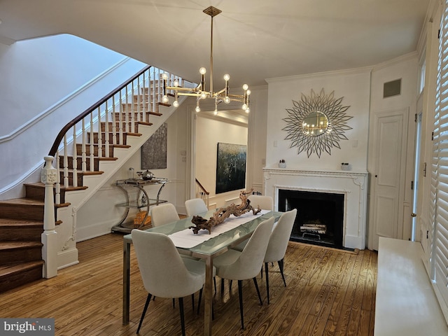 dining space with hardwood / wood-style floors, ornamental molding, and an inviting chandelier