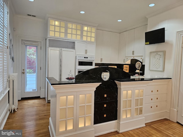 kitchen featuring white double oven, white cabinets, light hardwood / wood-style floors, crown molding, and radiator