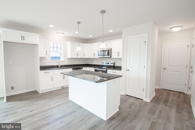 kitchen with appliances with stainless steel finishes, sink, a kitchen island, hanging light fixtures, and white cabinetry