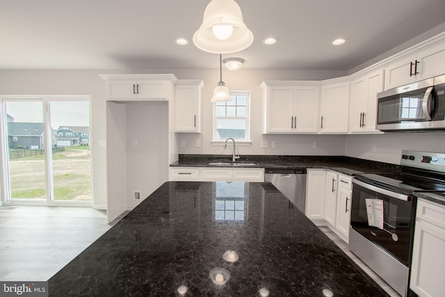 kitchen with white cabinets, appliances with stainless steel finishes, dark stone countertops, pendant lighting, and sink