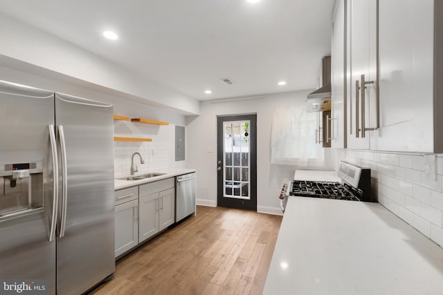 kitchen featuring appliances with stainless steel finishes, backsplash, light hardwood / wood-style floors, wall chimney range hood, and sink