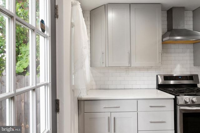 kitchen featuring wall chimney exhaust hood, plenty of natural light, stainless steel range with gas stovetop, and tasteful backsplash