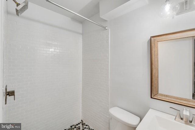 bathroom with sink, a tile shower, and toilet