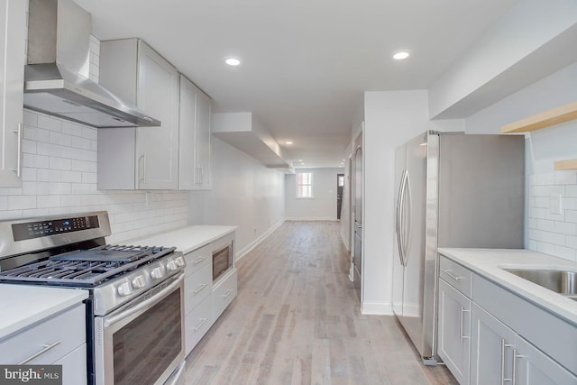 kitchen with wall chimney exhaust hood, tasteful backsplash, light hardwood / wood-style flooring, and stainless steel appliances