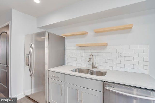 kitchen with light stone countertops, backsplash, appliances with stainless steel finishes, sink, and hardwood / wood-style flooring