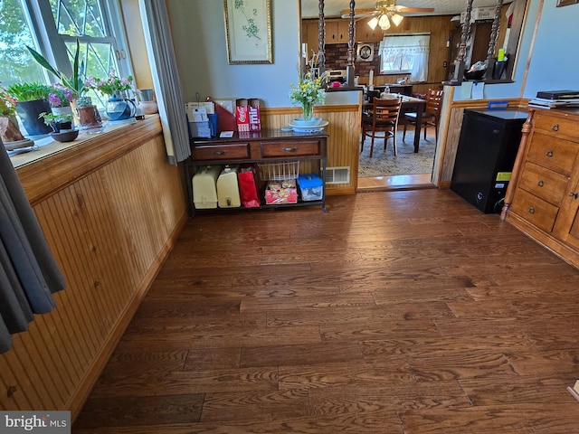 interior space featuring ceiling fan, dark wood-type flooring, and wooden walls