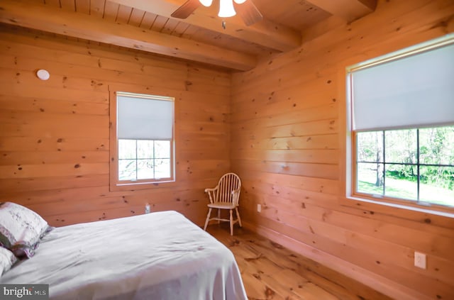 bedroom with ceiling fan, hardwood / wood-style floors, beamed ceiling, and wooden walls