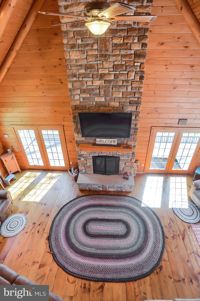 unfurnished living room with high vaulted ceiling, light hardwood / wood-style flooring, beam ceiling, and wooden walls