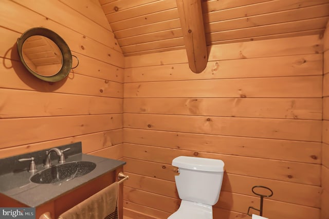 bathroom featuring vaulted ceiling, vanity, toilet, and wooden walls