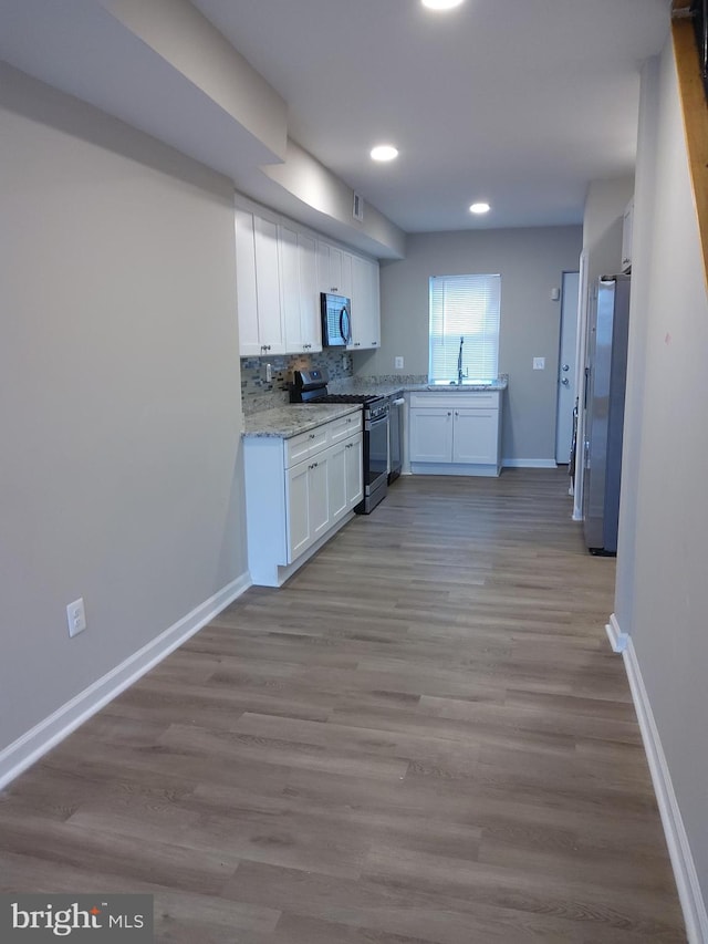 kitchen with white cabinets, sink, light hardwood / wood-style flooring, light stone countertops, and appliances with stainless steel finishes