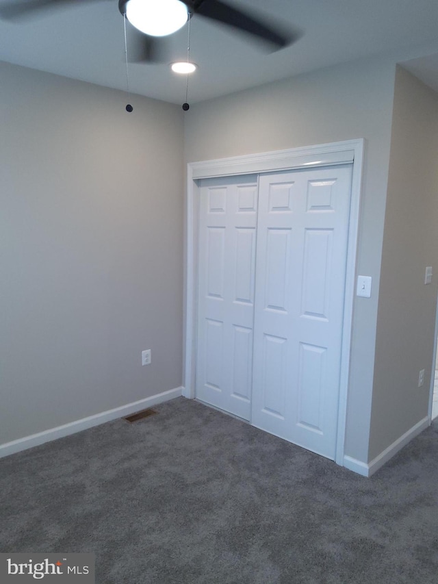 unfurnished bedroom with ceiling fan, a closet, and dark carpet