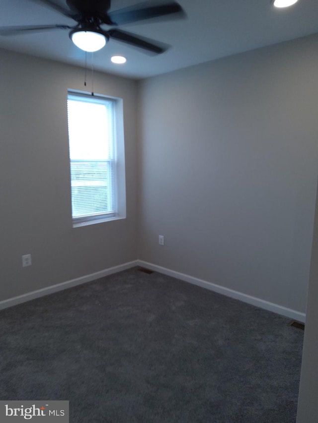 spare room featuring ceiling fan and dark colored carpet