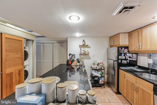 kitchen with light tile flooring, stacked washer / dryer, sink, dark stone counters, and stainless steel fridge