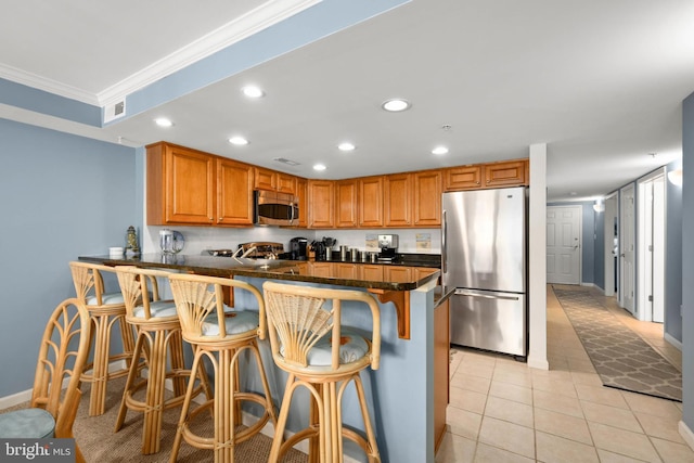 kitchen with stainless steel appliances, kitchen peninsula, crown molding, a breakfast bar area, and light tile patterned floors