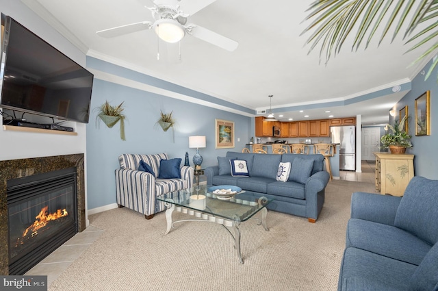 living room featuring ceiling fan, ornamental molding, light carpet, and a tiled fireplace