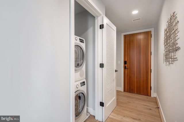 laundry room featuring stacked washer / dryer and light hardwood / wood-style flooring