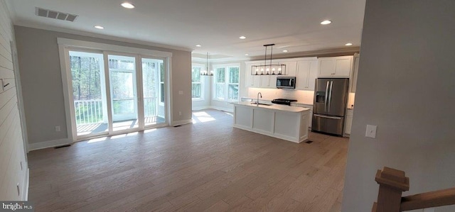 kitchen with decorative light fixtures, appliances with stainless steel finishes, hardwood / wood-style flooring, and a kitchen island with sink