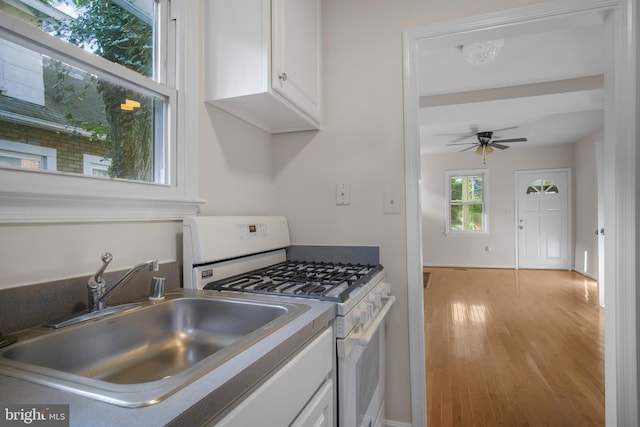 kitchen featuring ceiling fan, white cabinetry, white gas range, sink, and light wood-type flooring