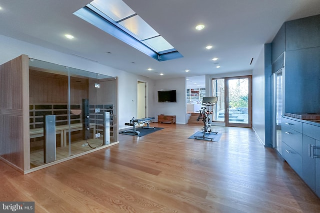 exercise room with a skylight and light wood-type flooring