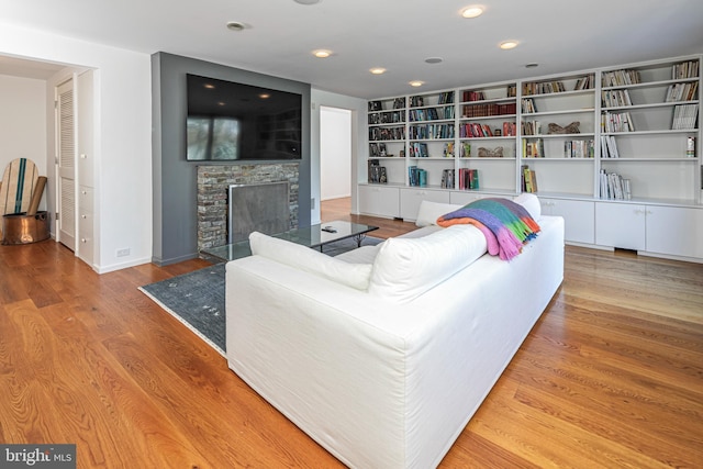 living room with light hardwood / wood-style floors, built in shelves, and a stone fireplace