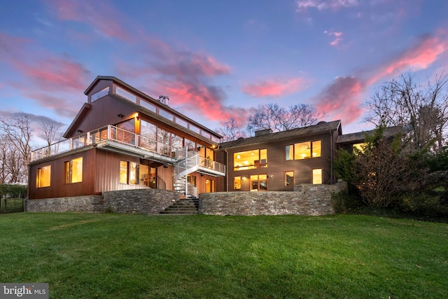 back house at dusk featuring a balcony and a yard