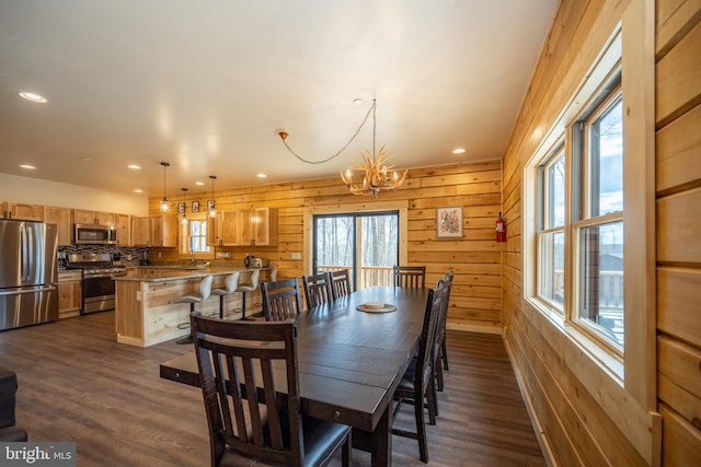 dining area with a chandelier, dark wood-type flooring, and wooden walls