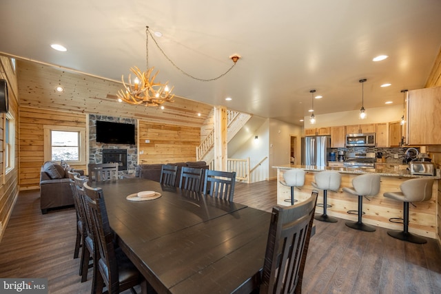 dining room with wood walls, a stone fireplace, an inviting chandelier, and dark hardwood / wood-style floors