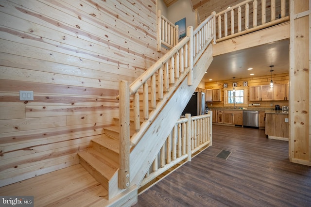 stairway with sink, dark wood-type flooring, and wooden walls