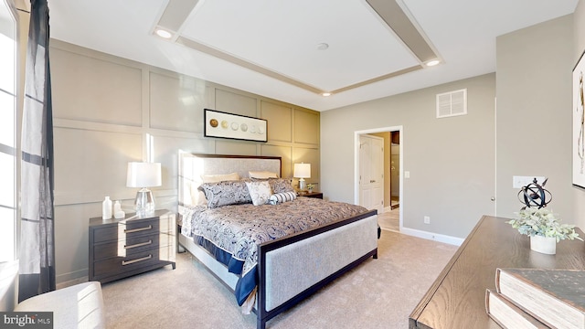 bedroom featuring a raised ceiling and light carpet