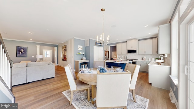 dining space with ornamental molding, sink, a notable chandelier, and light wood-type flooring