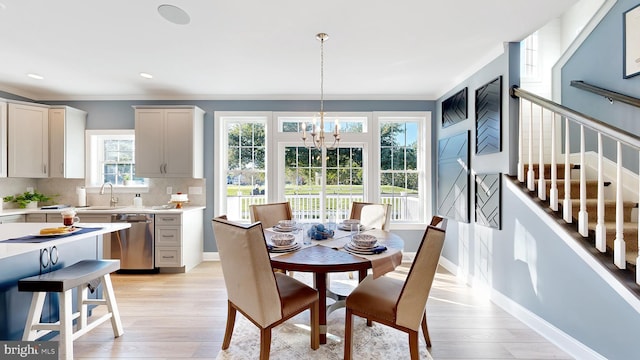 dining space featuring sink, light hardwood / wood-style flooring, a chandelier, and crown molding