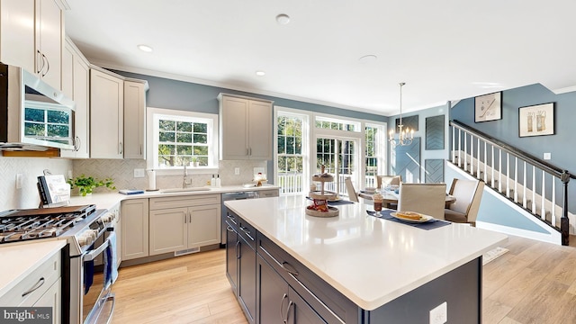 kitchen featuring appliances with stainless steel finishes, backsplash, light hardwood / wood-style floors, a center island, and an inviting chandelier