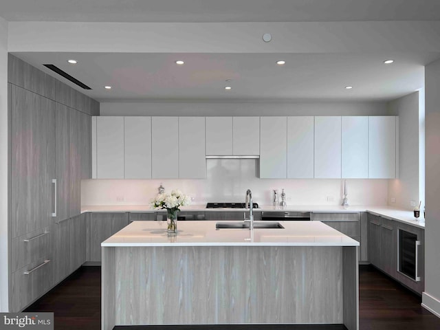 kitchen with sink, dark wood-type flooring, wine cooler, and a center island with sink