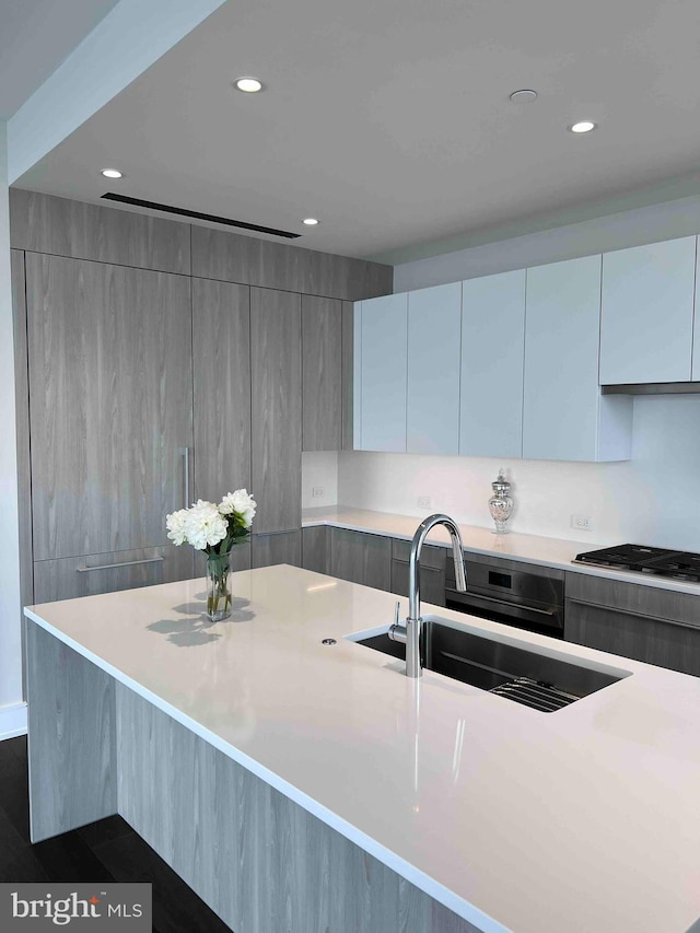 kitchen featuring stainless steel gas cooktop, a spacious island, sink, and dark wood-type flooring