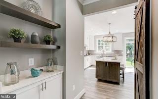 bar featuring a barn door, white cabinetry, pendant lighting, and light hardwood / wood-style floors