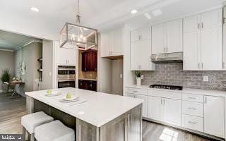 kitchen with white cabinets, light hardwood / wood-style flooring, appliances with stainless steel finishes, decorative light fixtures, and a kitchen island