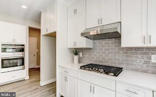 kitchen featuring white cabinets, light wood-type flooring, appliances with stainless steel finishes, and tasteful backsplash