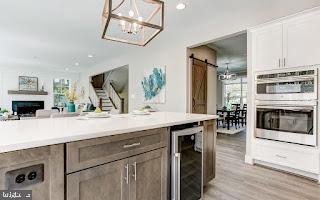 kitchen featuring stainless steel double oven, beverage cooler, a barn door, light hardwood / wood-style flooring, and white cabinets