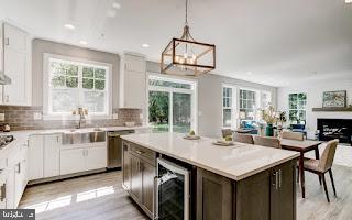 kitchen with decorative light fixtures, wine cooler, light hardwood / wood-style floors, and white cabinetry