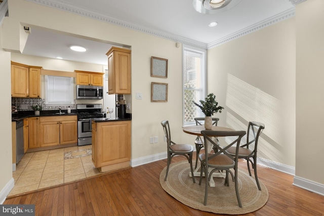 kitchen with crown molding, decorative backsplash, stainless steel appliances, and light wood-type flooring